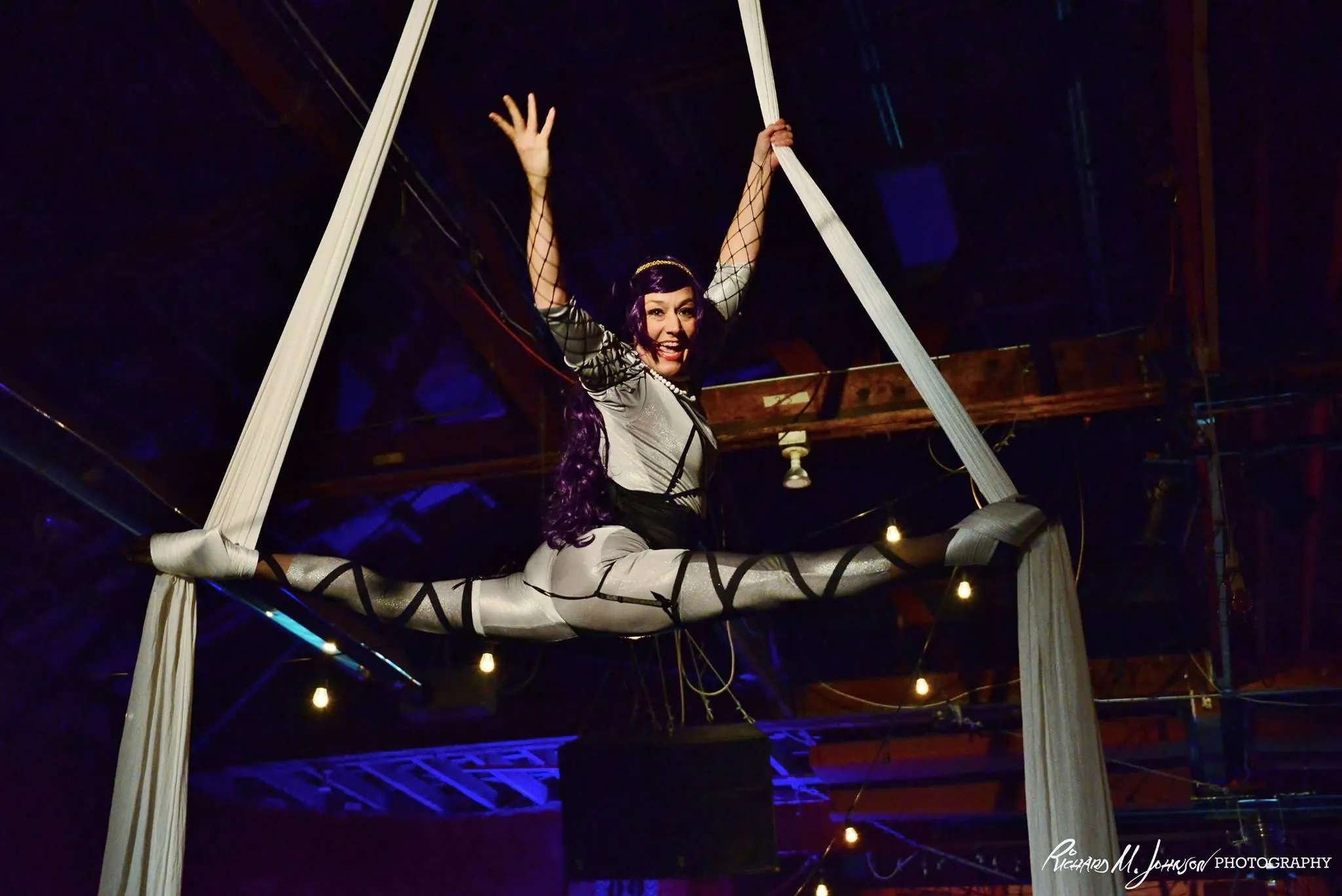 Aerialist in a split on silks hung from the bow truss ceiling