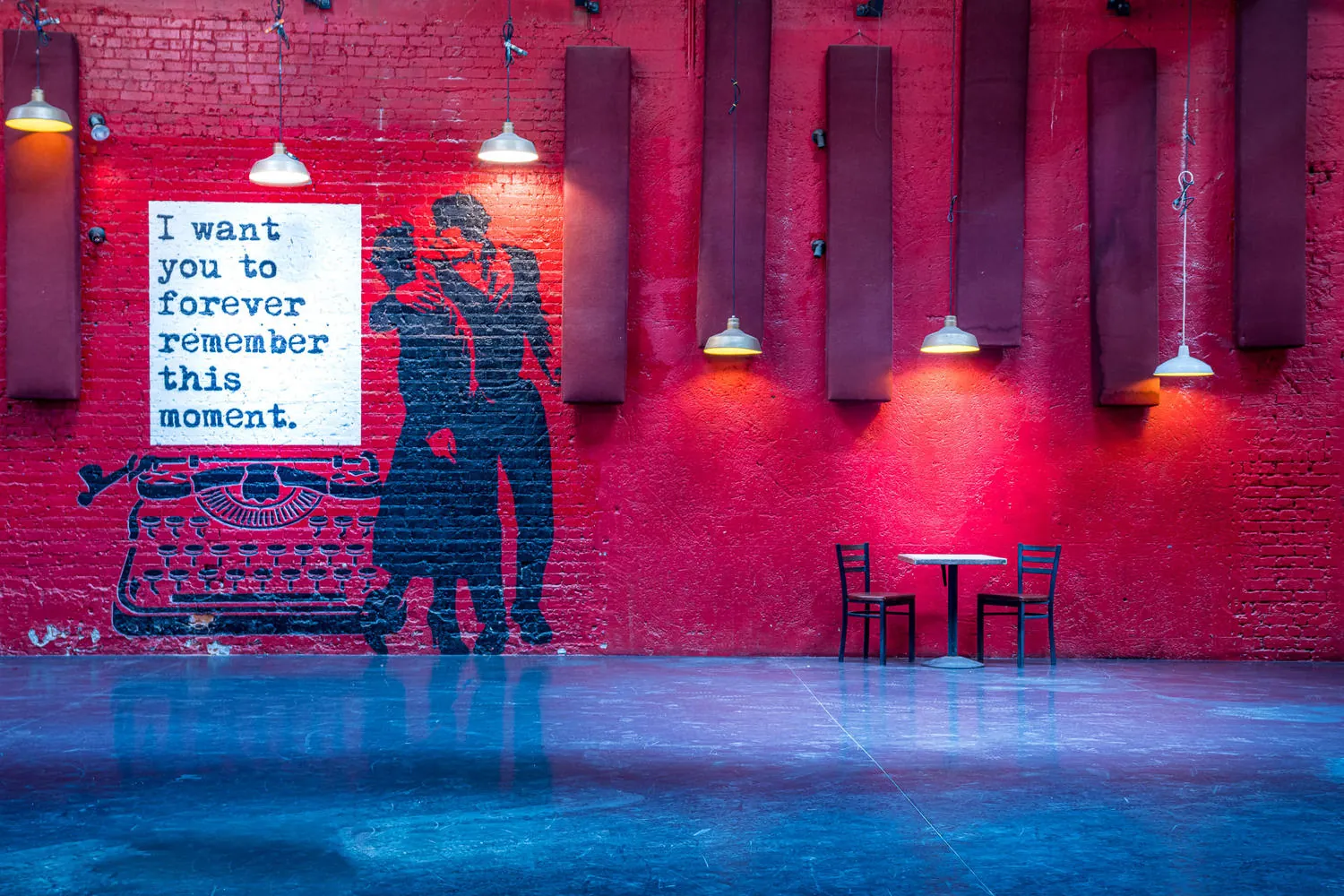 Red brick wall with pendant lights, cafe tables and a mural